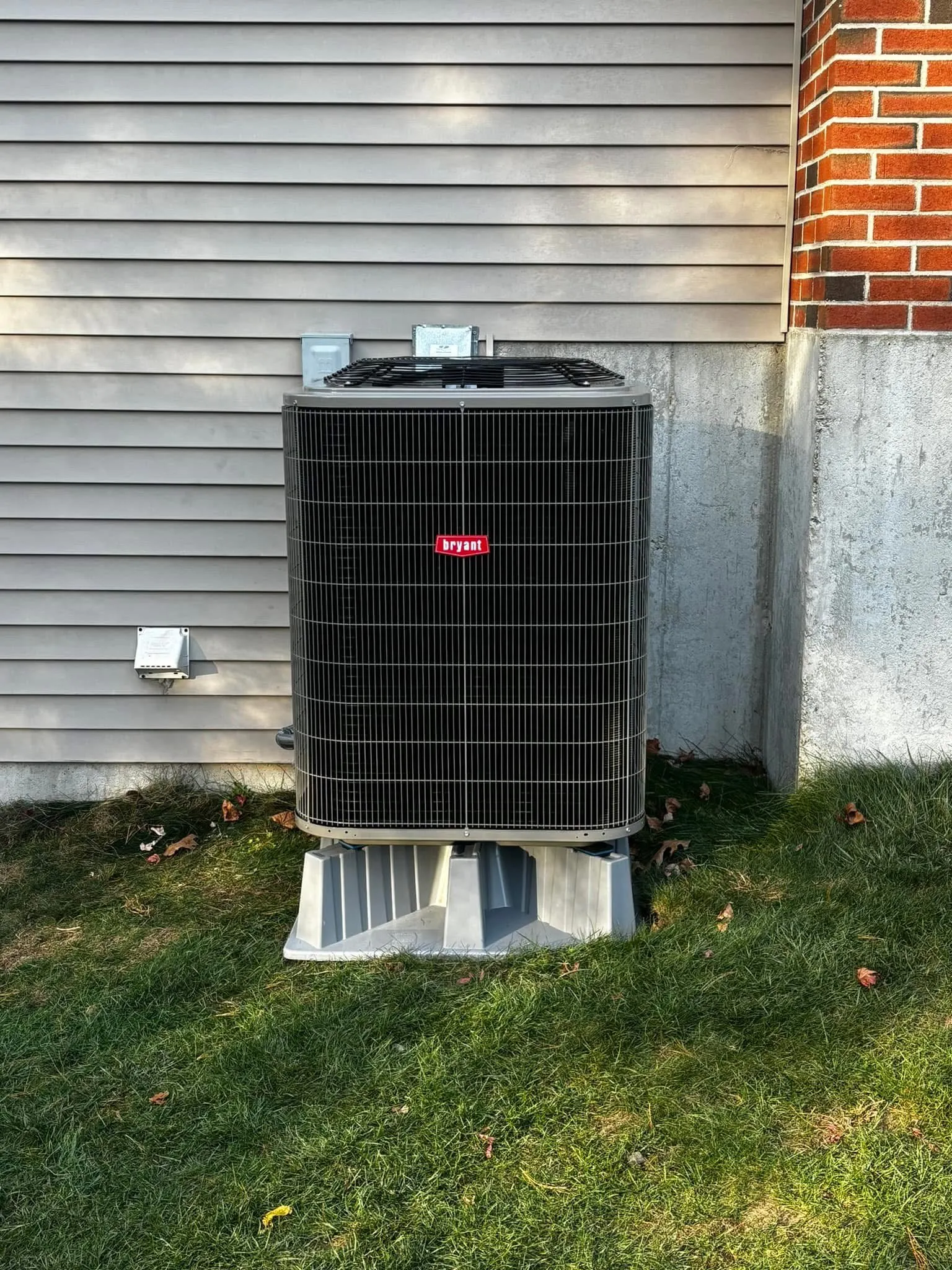 Bryant air conditioning condenser on a composite pad beside a brick chimney