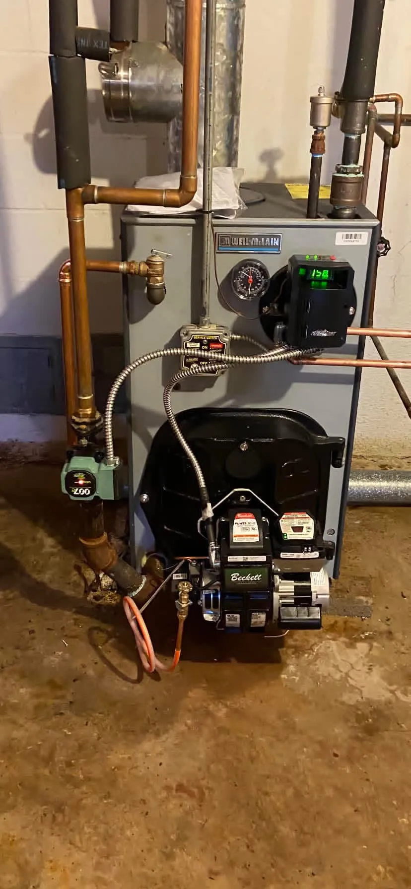 Close-up of a Weil-McLain oil boiler serviced by Hannon, with a Beckett PowerLight burner, green Taco circulator, and HydroStat control