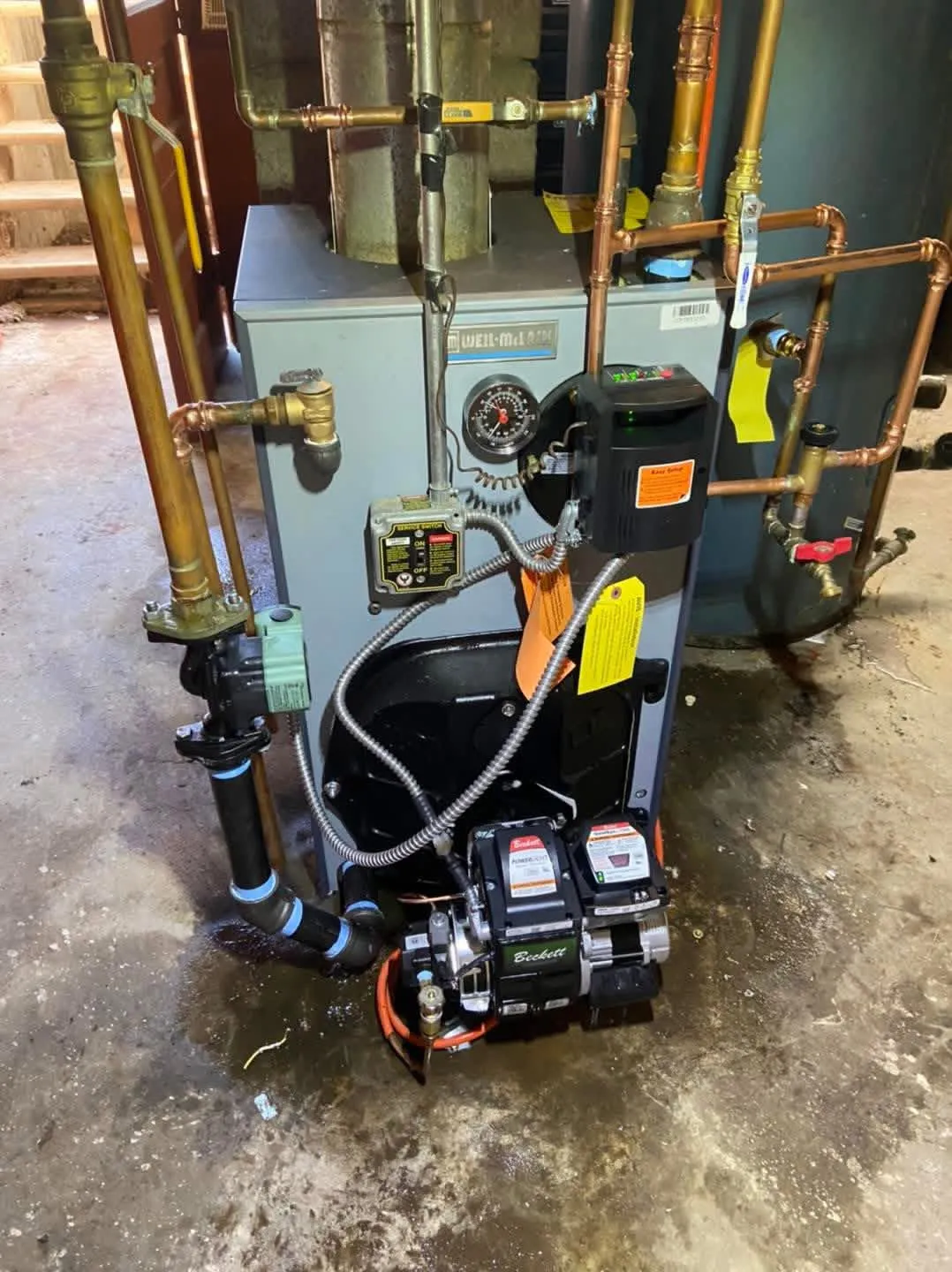 Weil-McLain boiler with a Beckett burner mid-install in an older basement, brass and copper piping overhead