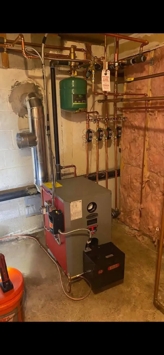 Copper zone manifold with green Taco circulators and a Hannon service tag on a new oil boiler installation