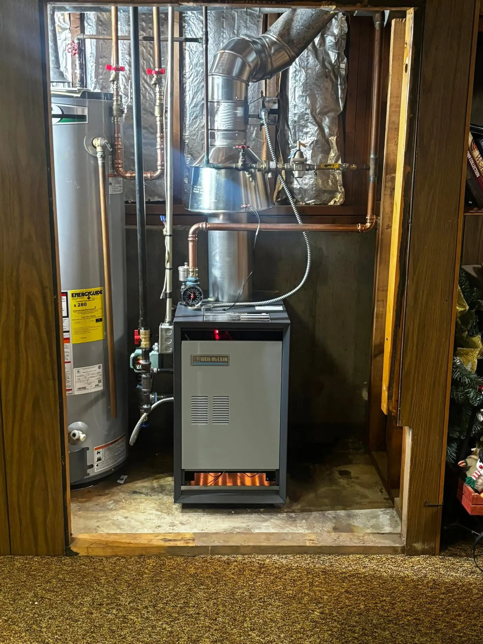 Weil-McLain gas boiler running in a wood-paneled utility closet beside a gas water heater