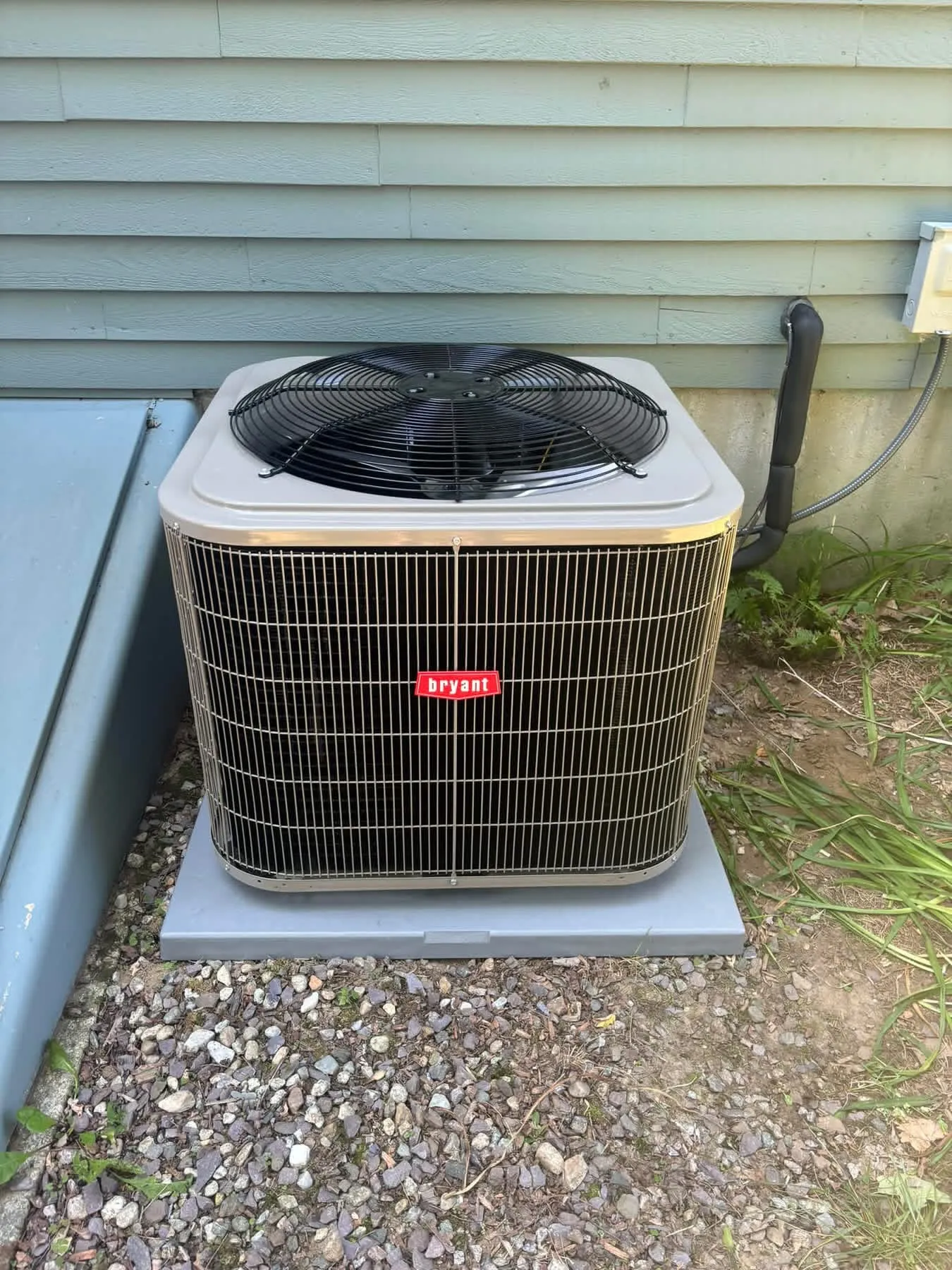 Bryant outdoor unit installed on a pad beside a home with sage-green clapboard siding
